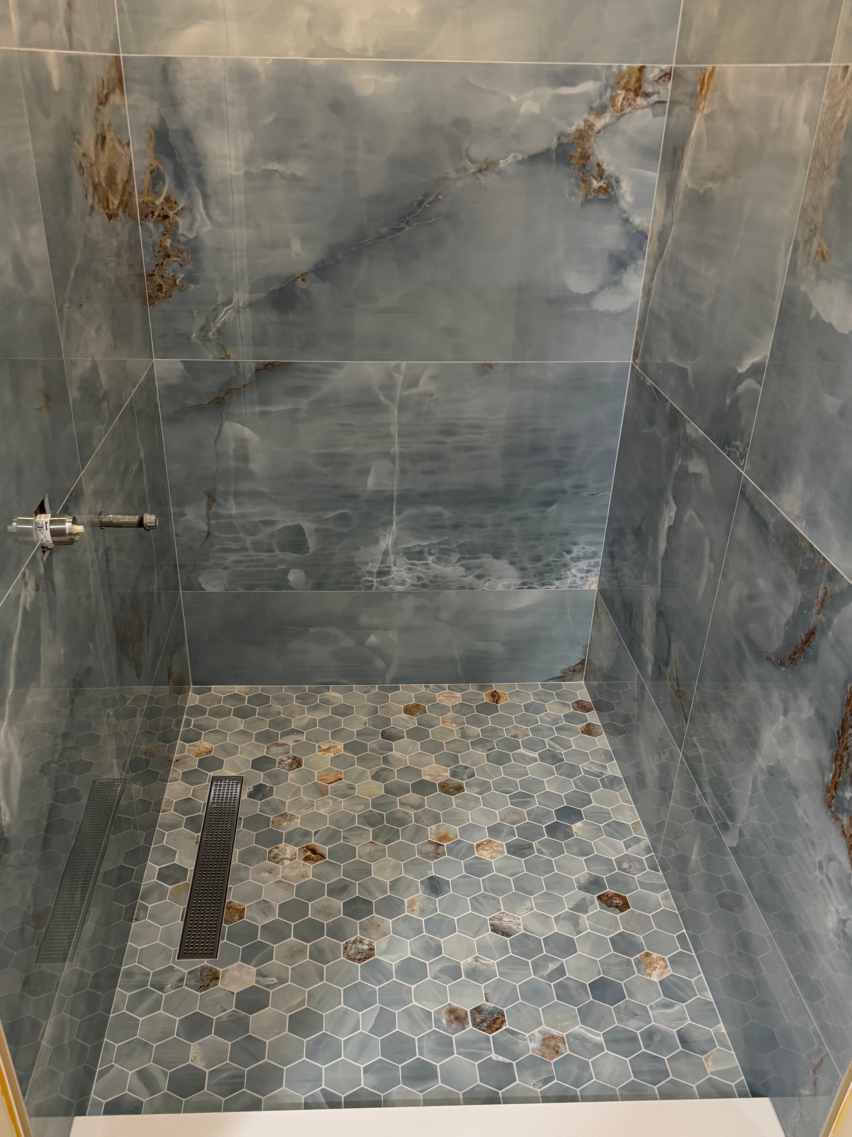 Bathroom walk-in shower with blue marble-look wall tile and hexagon mosaic floor