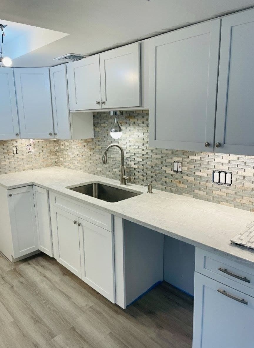 White kitchen cabinets with a mosaic tile backsplash and wood-look floor